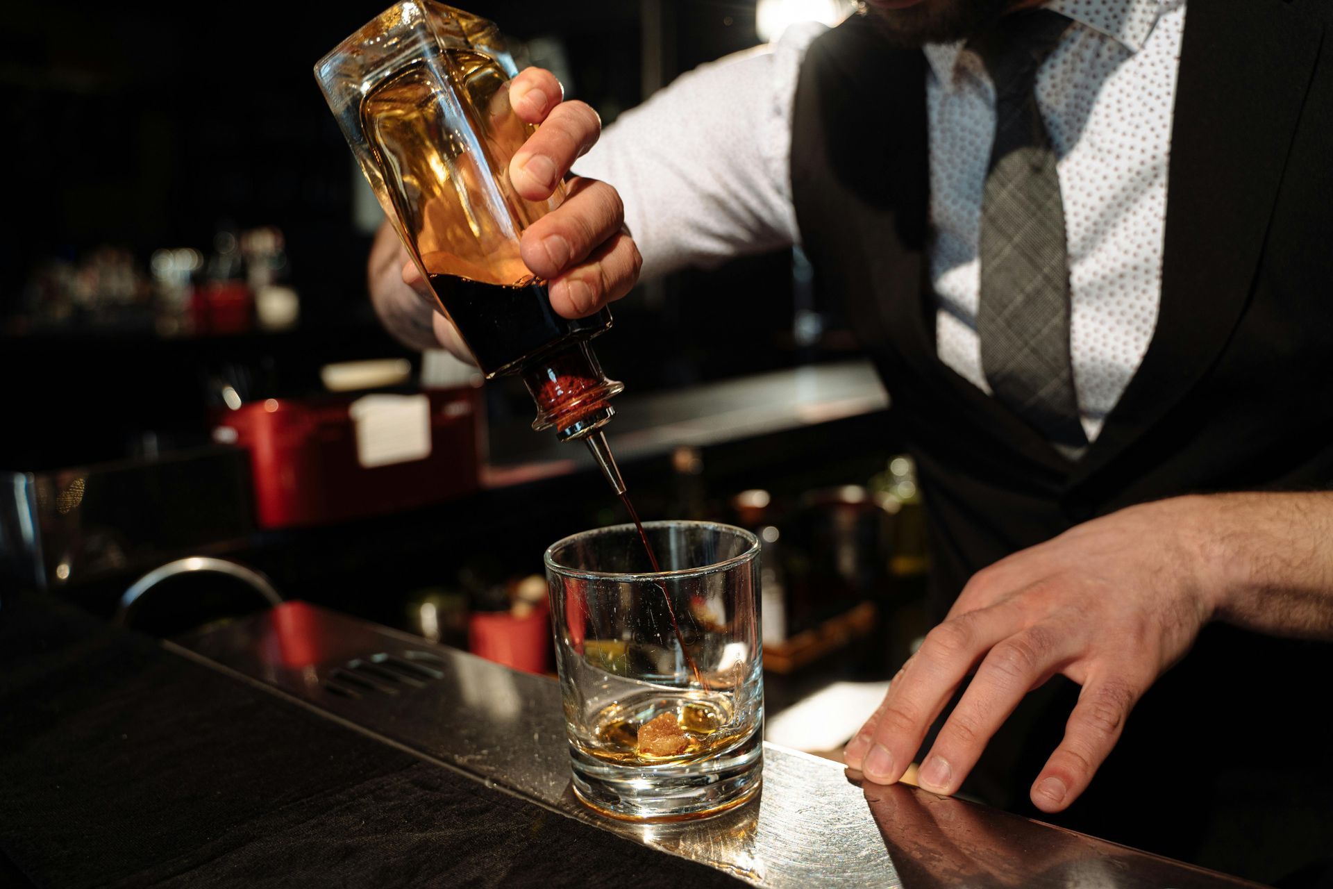 Bartender pouring amber liquor into a short glass at a dimly lit bar.