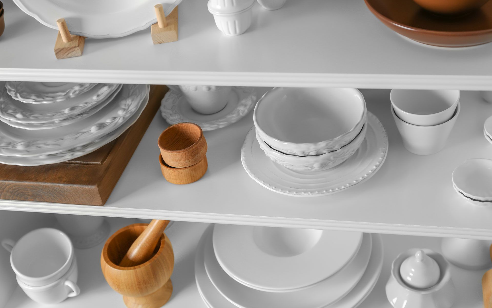 A shelf filled with plates , bowls , cups , and a mortar and pestle.