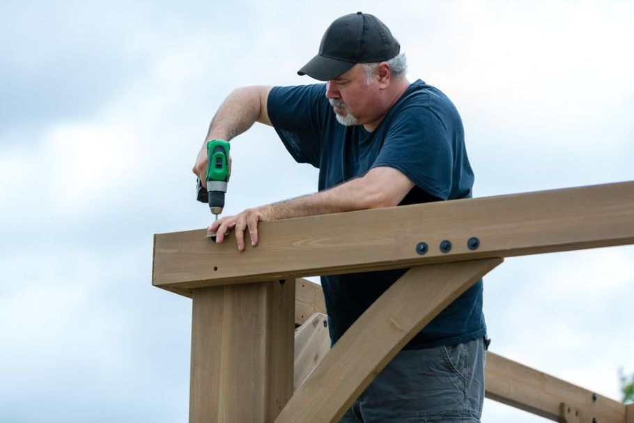 Man using a green drill to fasten a wooden beam on a construction frame outdoors