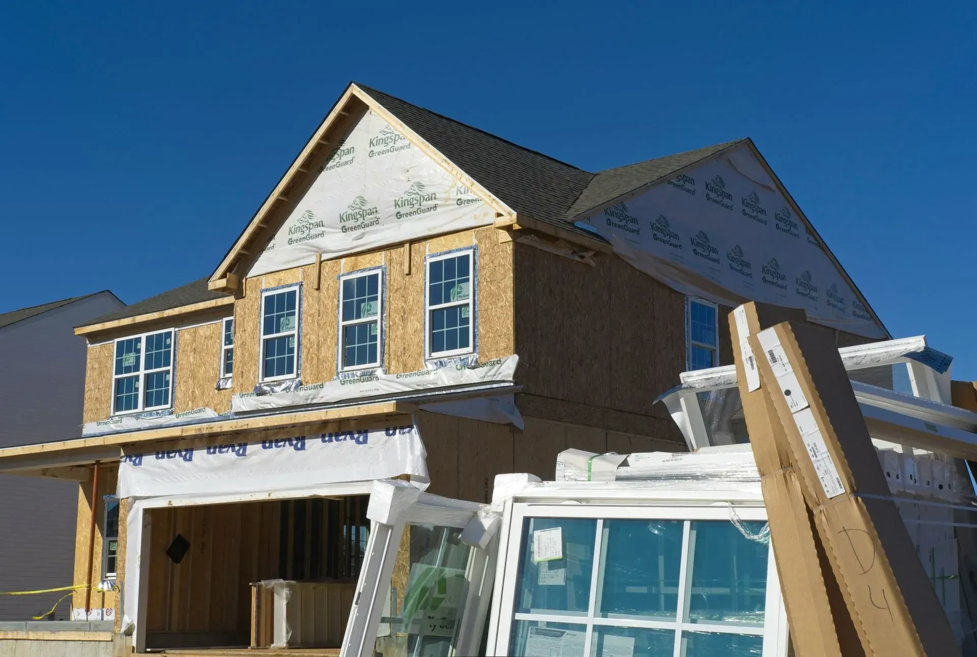 Partially built house under construction with exposed wood framing and windows against a clear blue sky