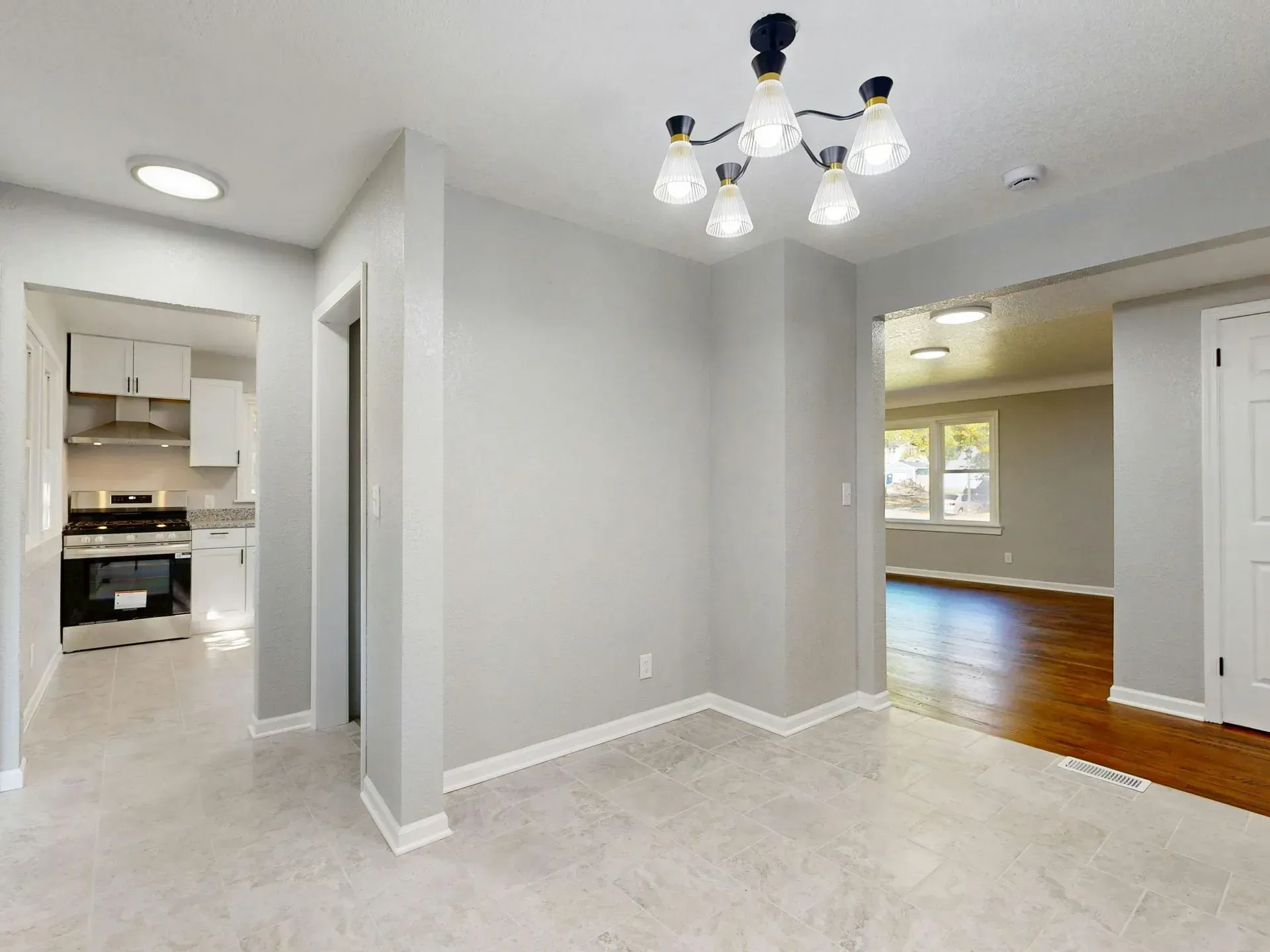 Empty dining area with beige carpet, gray walls, and an open view into a kitchen and hardwood-floored room
