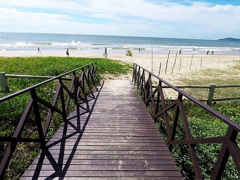Uma passarela de madeira que leva a uma praia com pessoas caminhando nela