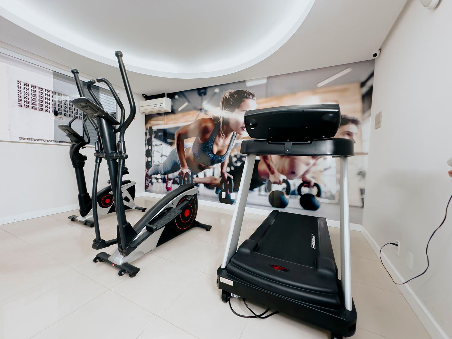 Uma academia com esteira, elíptico e outros equipamentos de exercício.