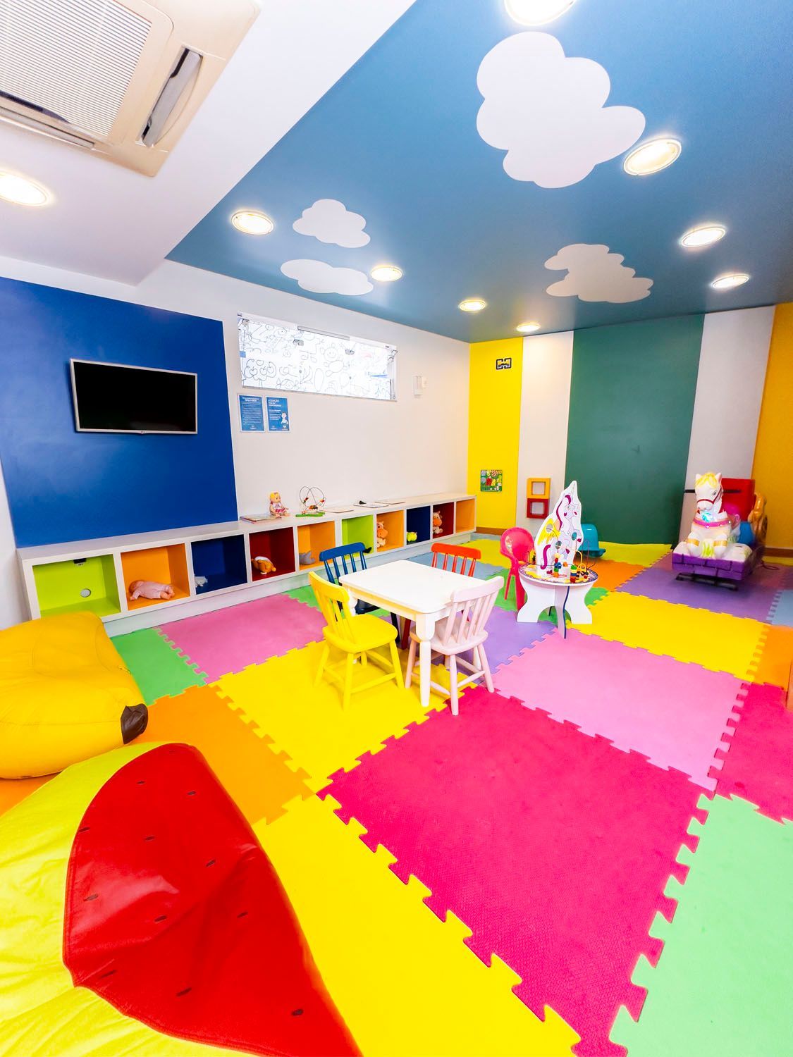 Uma sala de jogos colorida com mesas e cadeiras e uma TV na parede.