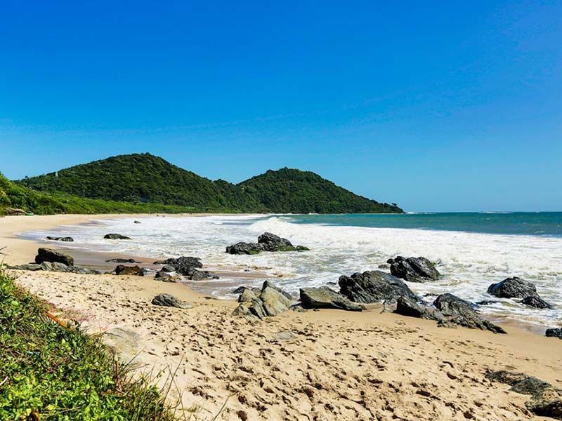 Uma praia de areia com pedras e montanhas ao fundo