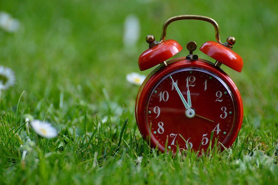 red alarm clock that shows five minutes to twelve