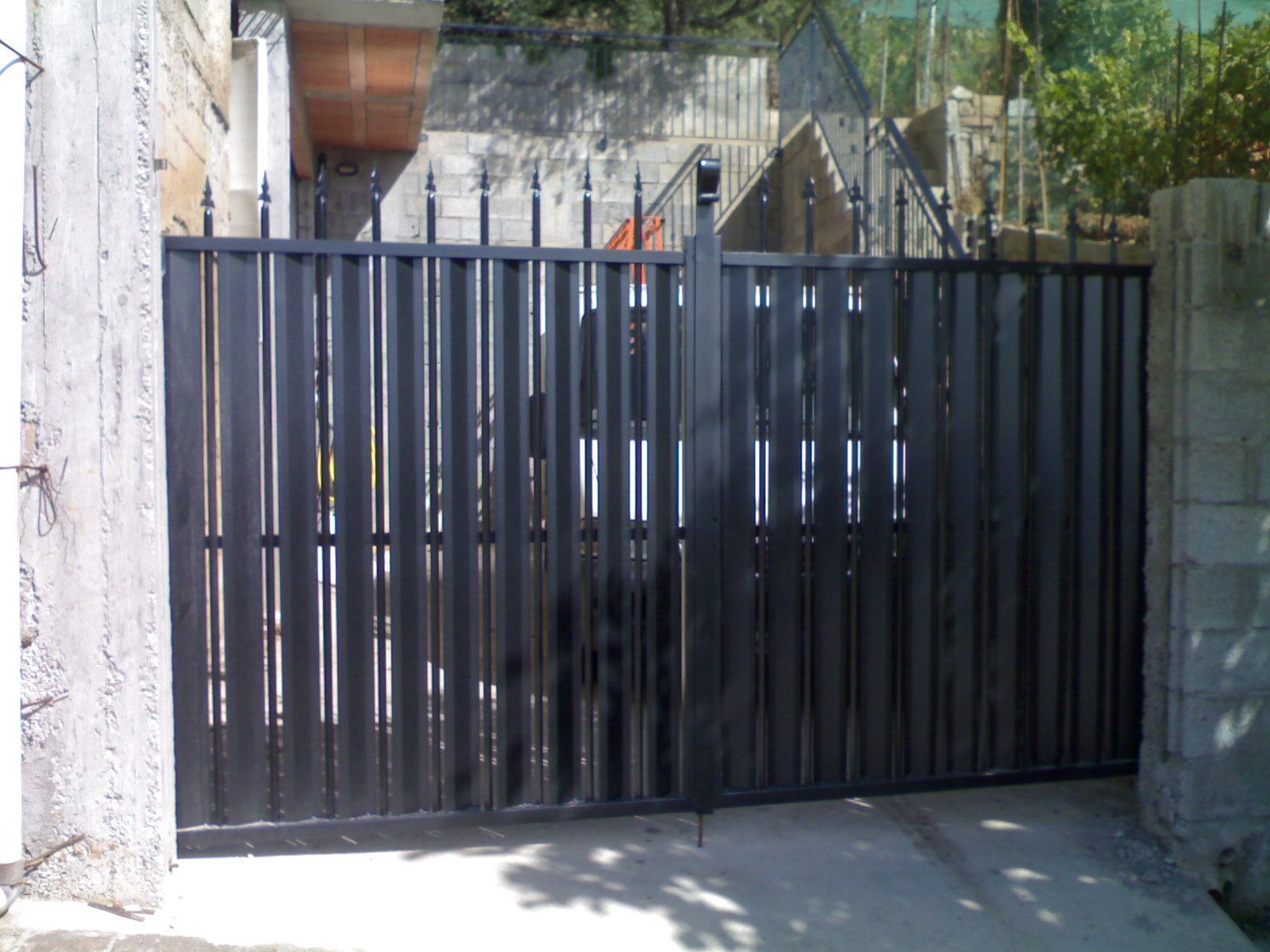 Cancello carrabile in metallo nero accanto a muri in pietra all'ingresso di una residenza