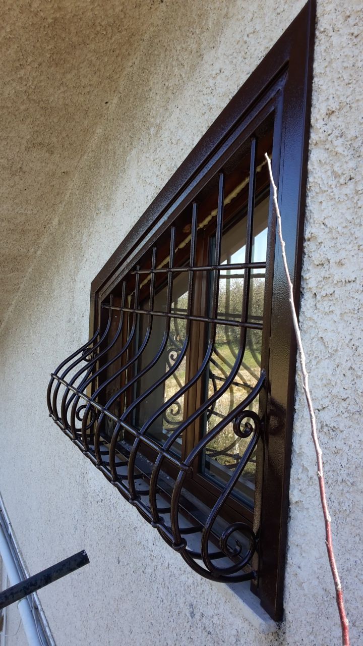 Finestra con sbarre su una parete di stucco beige, grata di sicurezza piegata e riflesso sul vetro.