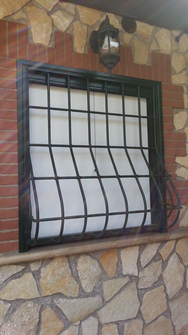 Finestra con tende bianche e sbarre nere incastonata in un muro di pietra e mattoni sotto una luce esterna