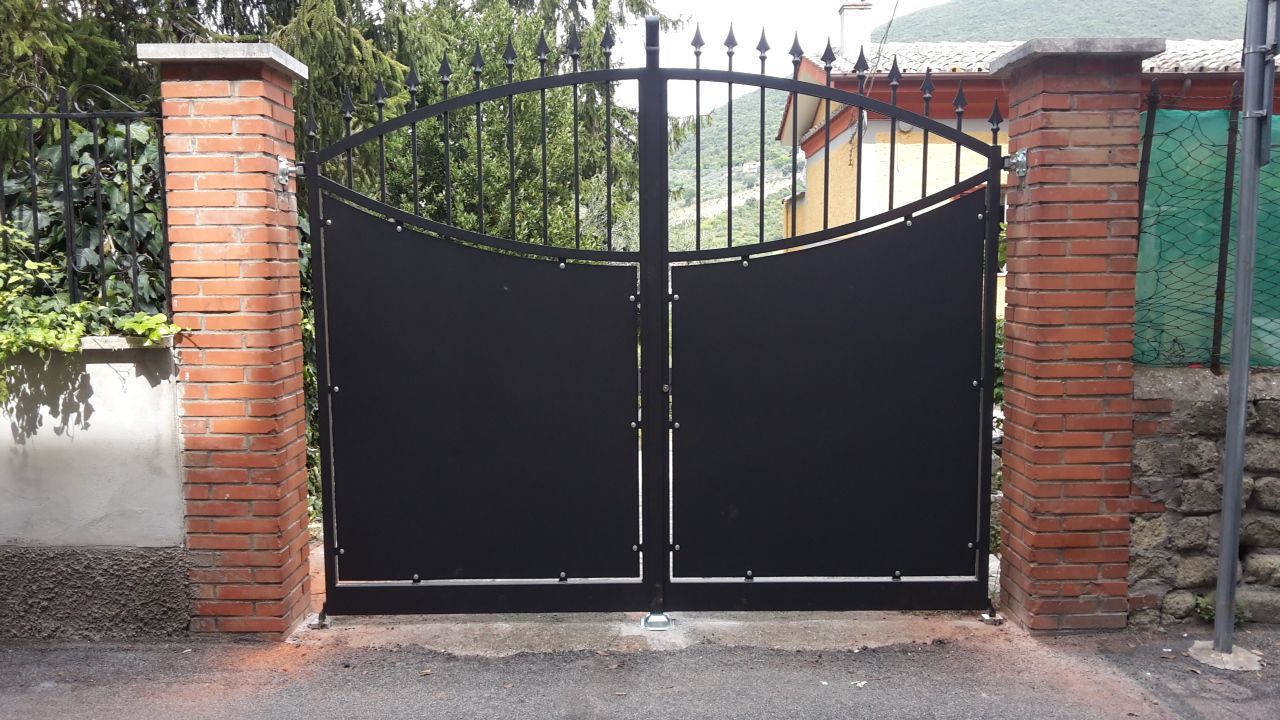 Cancello chiuso in metallo nero tra pilastri di mattoni rossi all'ingresso di un vialetto.