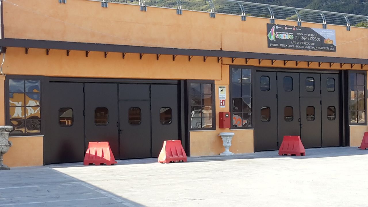 Edificio arancione con portoni scuri in stile garage e barriere rosse sul davanti, sotto un cielo soleggiato.