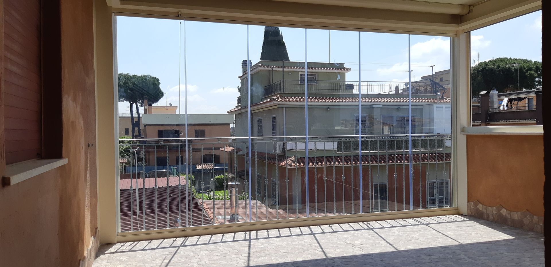 Vista da un balcone coperto con ringhiera in metallo che si affaccia su una piazza cittadina e su un edificio storico.