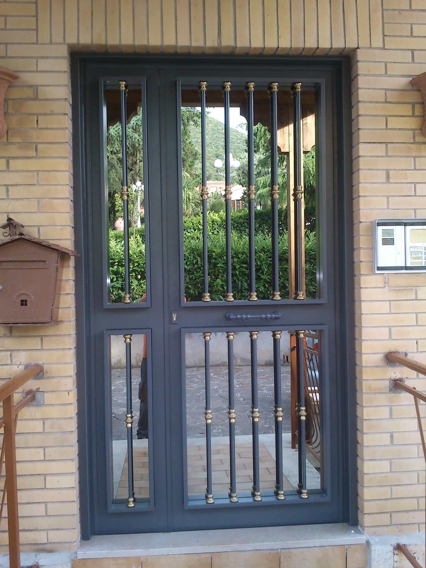 Porta blindata grigio scuro con sbarre, incastonata nell'ingresso di un edificio in mattoni.