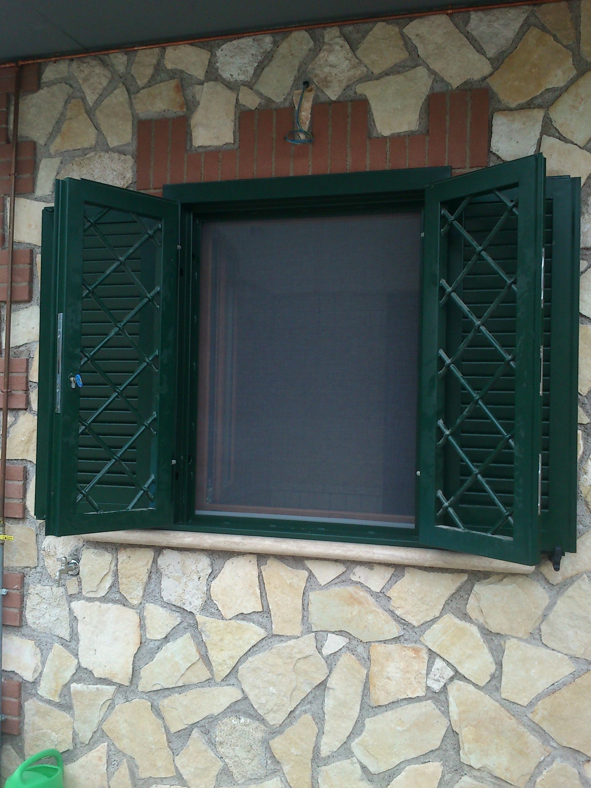 Finestra aperta con persiane verde scuro incastonata in un muro di pietra.