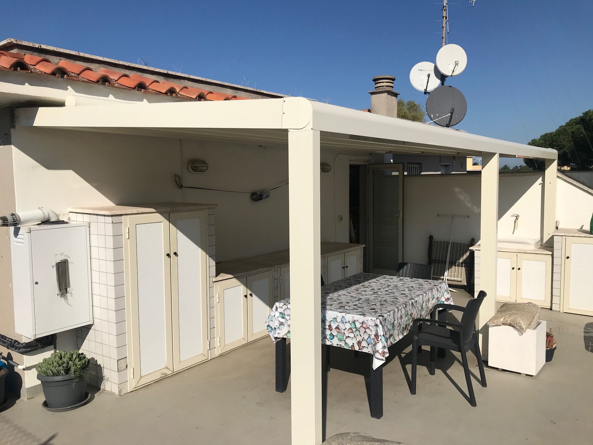 Patio con tavolo e sedie pieghevoli sotto una terrazza coperta accanto a una casa bianca