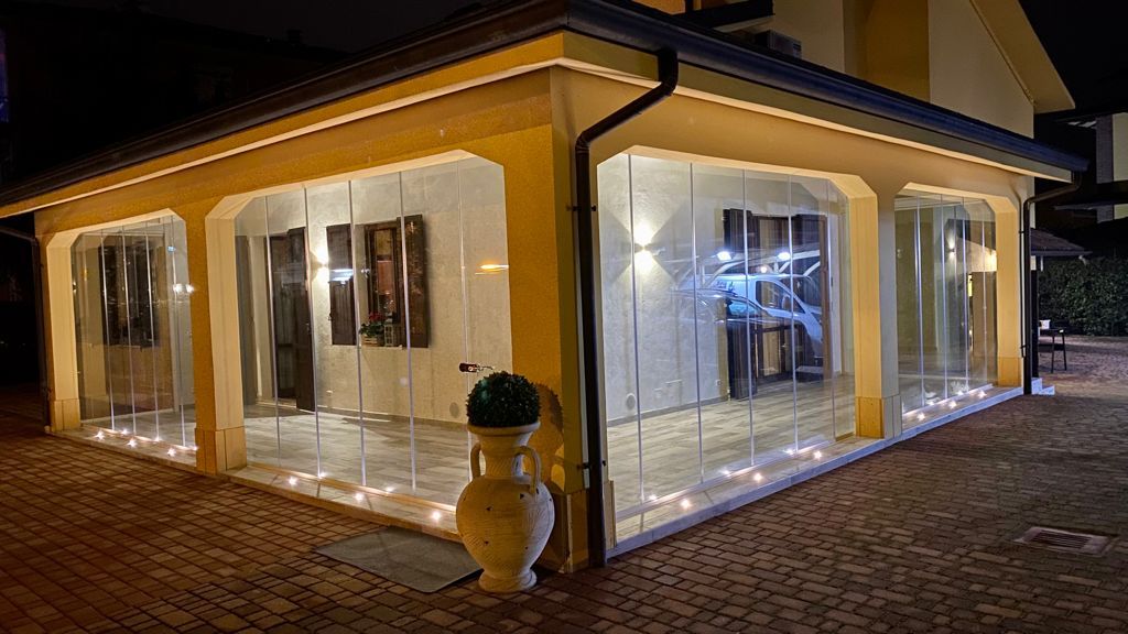 Casa moderna illuminata da una luce calda, di notte, con ampie vetrate e un patio piastrellato.