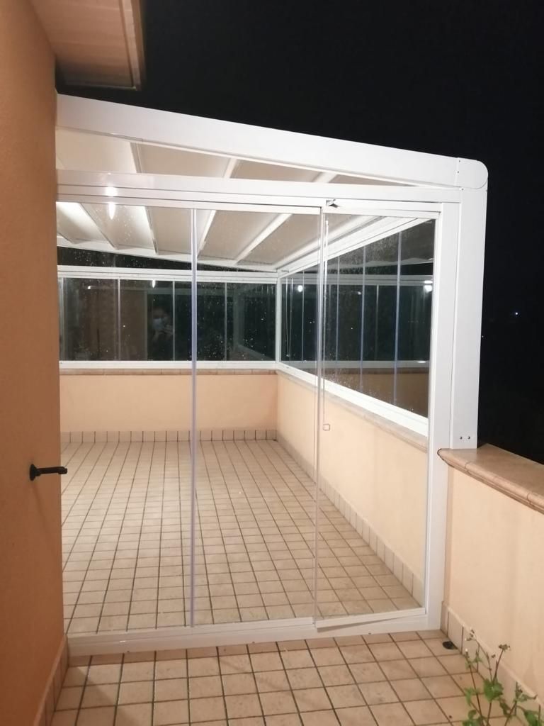 Balcone o veranda chiusa piastrellata, con pareti in vetro e struttura del tetto bianca, ideale per la notte.