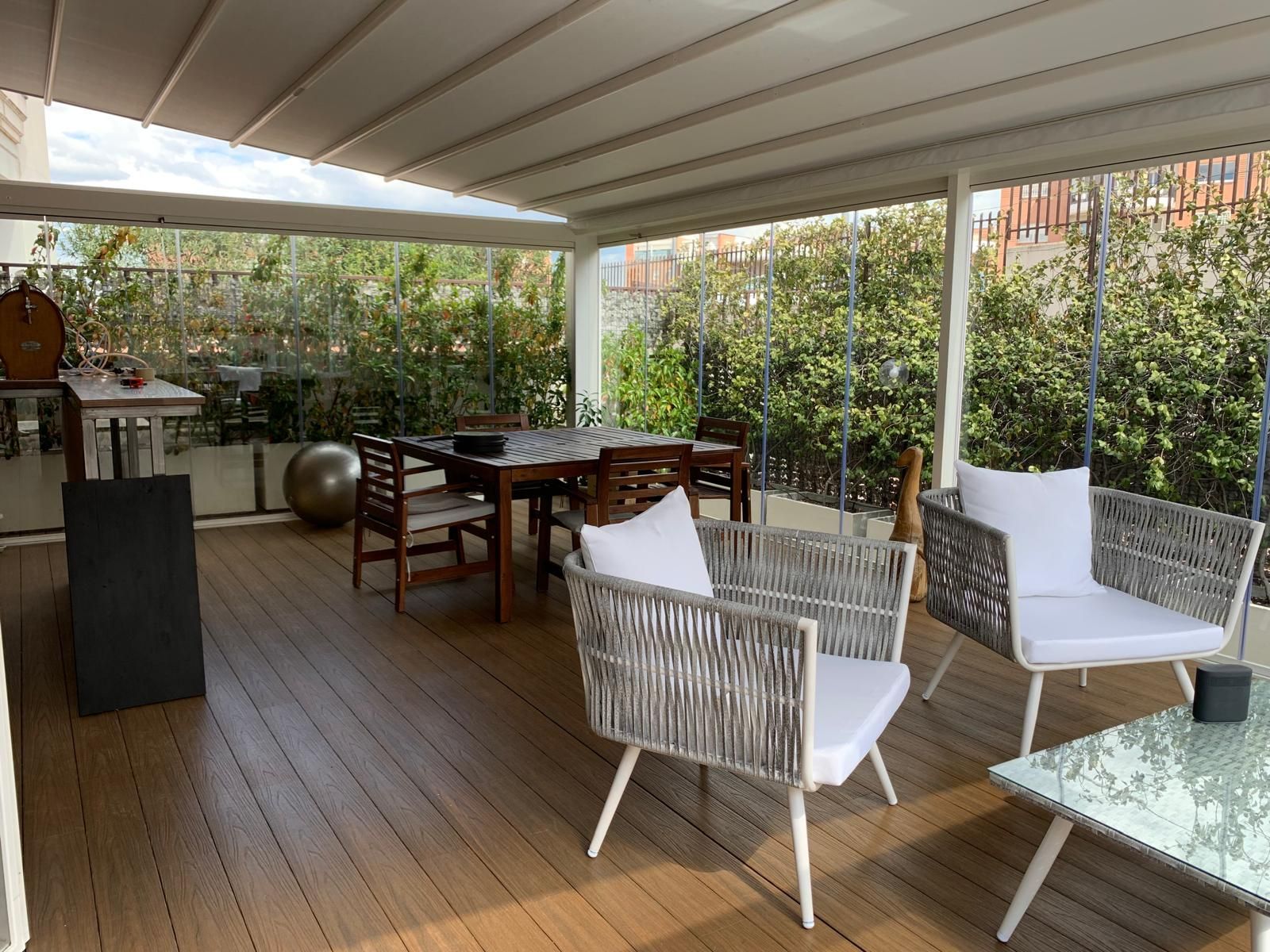 Patio coperto con sedie in vimini bianche, tavolo da pranzo in legno e piante in vaso, con vista sul giardino.
