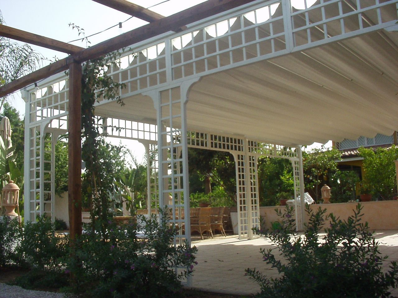Gazebo bianco a traliccio con tettoia drappeggiata in un patio da giardino.