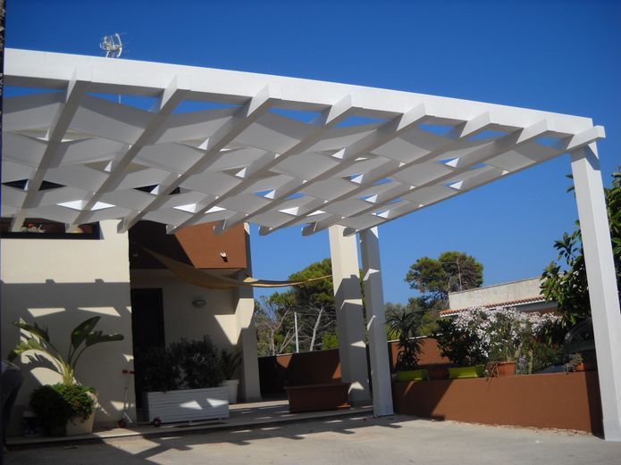 Patio di una casa moderna con pergola bianca, piante in vaso e un cielo azzurro limpido.