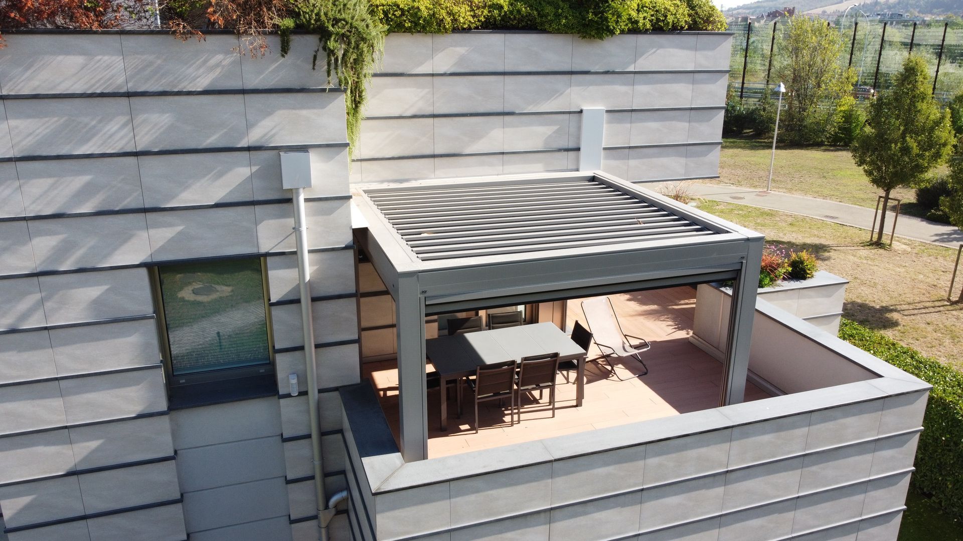 Terrazza panoramica moderna con pergola grigia, tavolo da pranzo all'aperto e rivestimento metallico circostante.