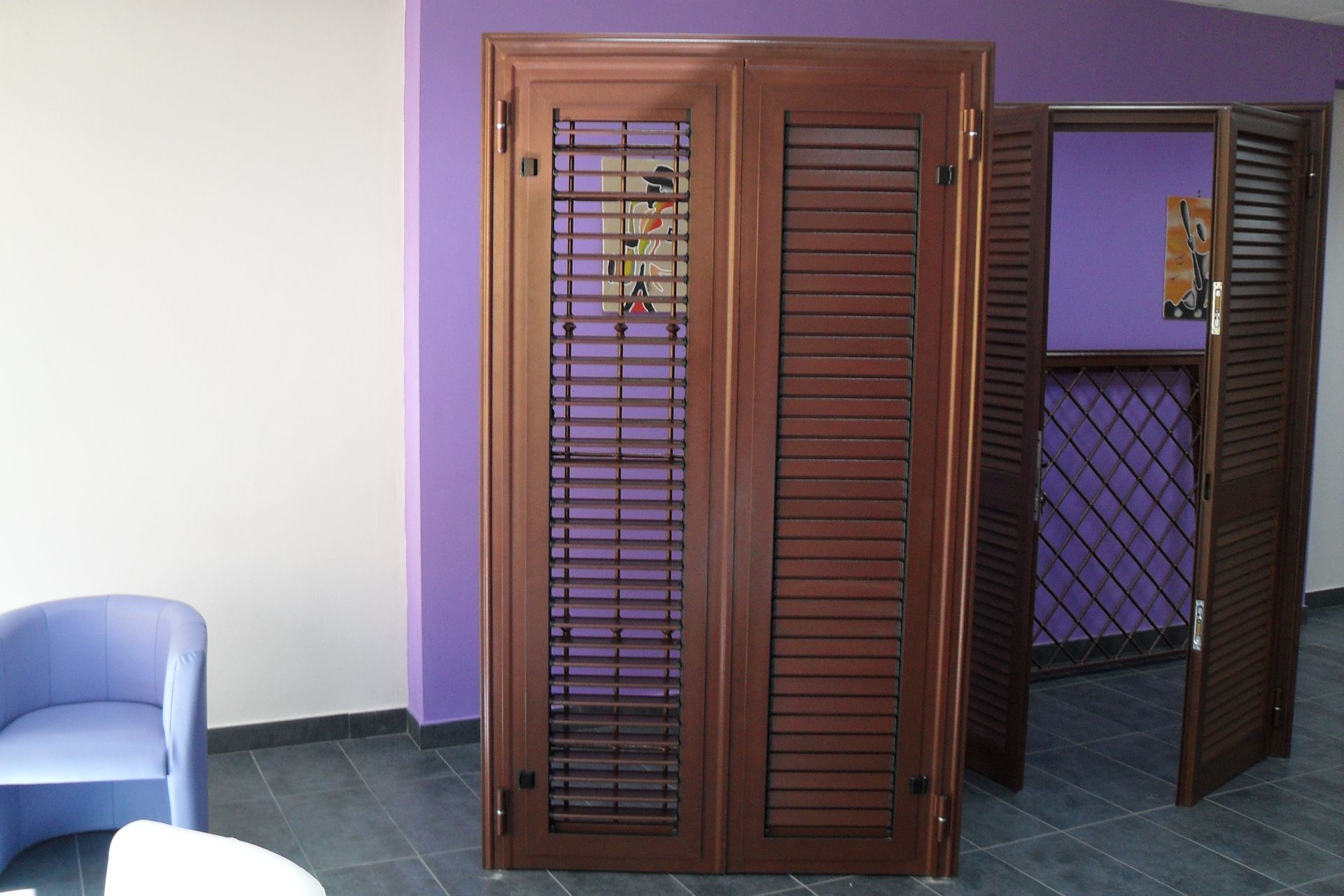 Porte a soffietto in legno in una stanza dalle pareti viola con una sedia blu sulla sinistra