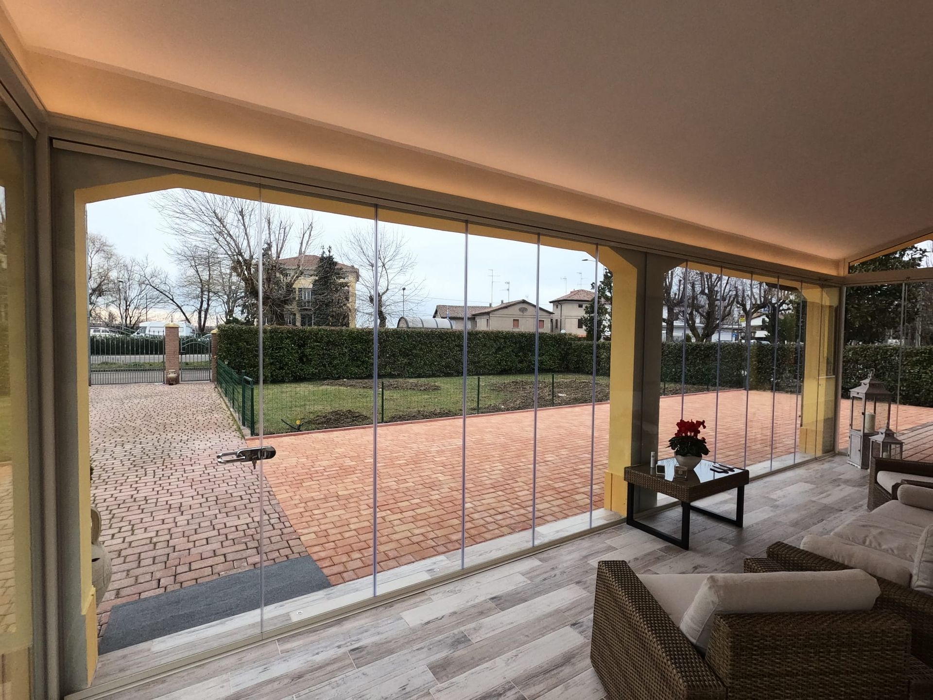 Patio moderno con ampie porte finestre che si aprono su un giardino curato e alberi all'esterno.