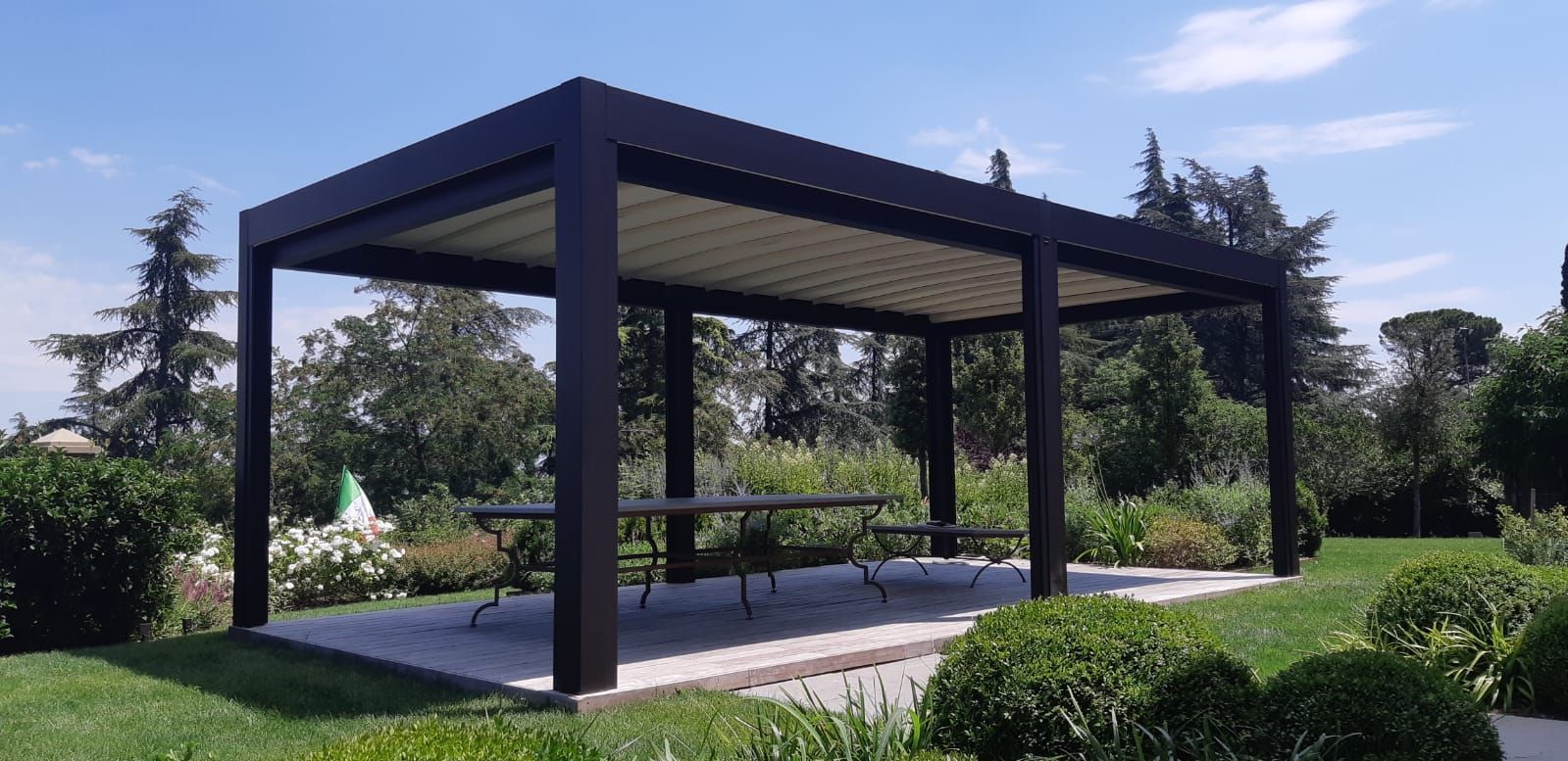 Gazebo in metallo scuro in un parco erboso con alberi e pavimento pavimentato