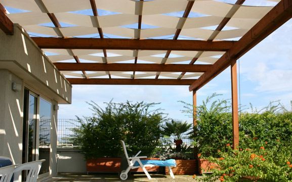 Patio soleggiato con pergolato in legno, sedie a sdraio e rigogliose piante in vaso con vista sul giardino.