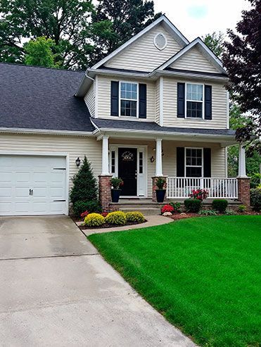 Suburban two-story house with white garage, front porch, and bright green lawn