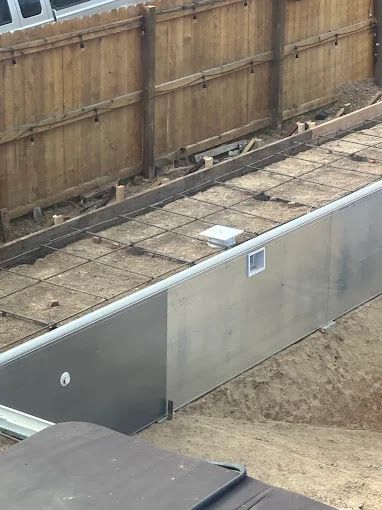 Outdoor construction area with a long concrete retaining wall and wooden fence behind it