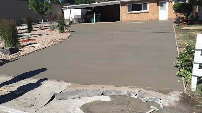 Freshly poured concrete driveway leading to a house with desert landscaping and a garage entrance