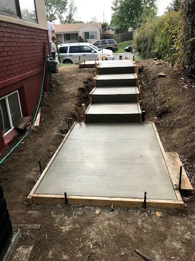 Concrete backyard steps and landing under construction beside a house and retaining wall