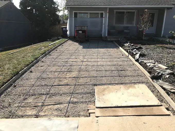 Concrete driveway under construction leading to a house, with rebar grid and a plywood board near the front.