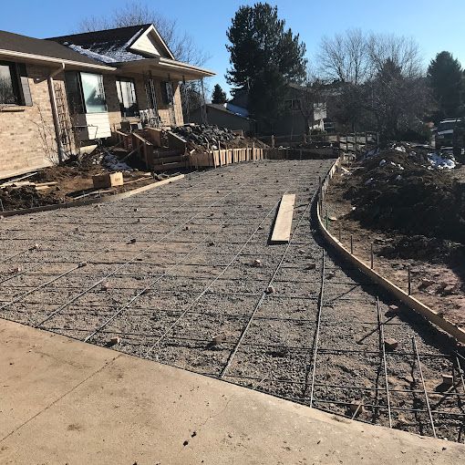 Construction site with a house, concrete walkway forms, and exposed rebar in a landscaped front yard.