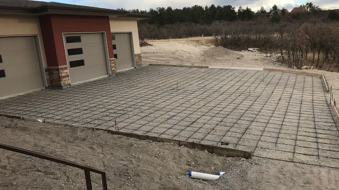 Paved patio with concrete grid pattern beside a garage, leading to a sandy, wooded yard
