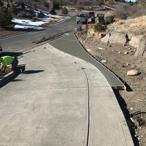 New concrete sidewalk along a curving road with roadwork equipment and snow patches nearby