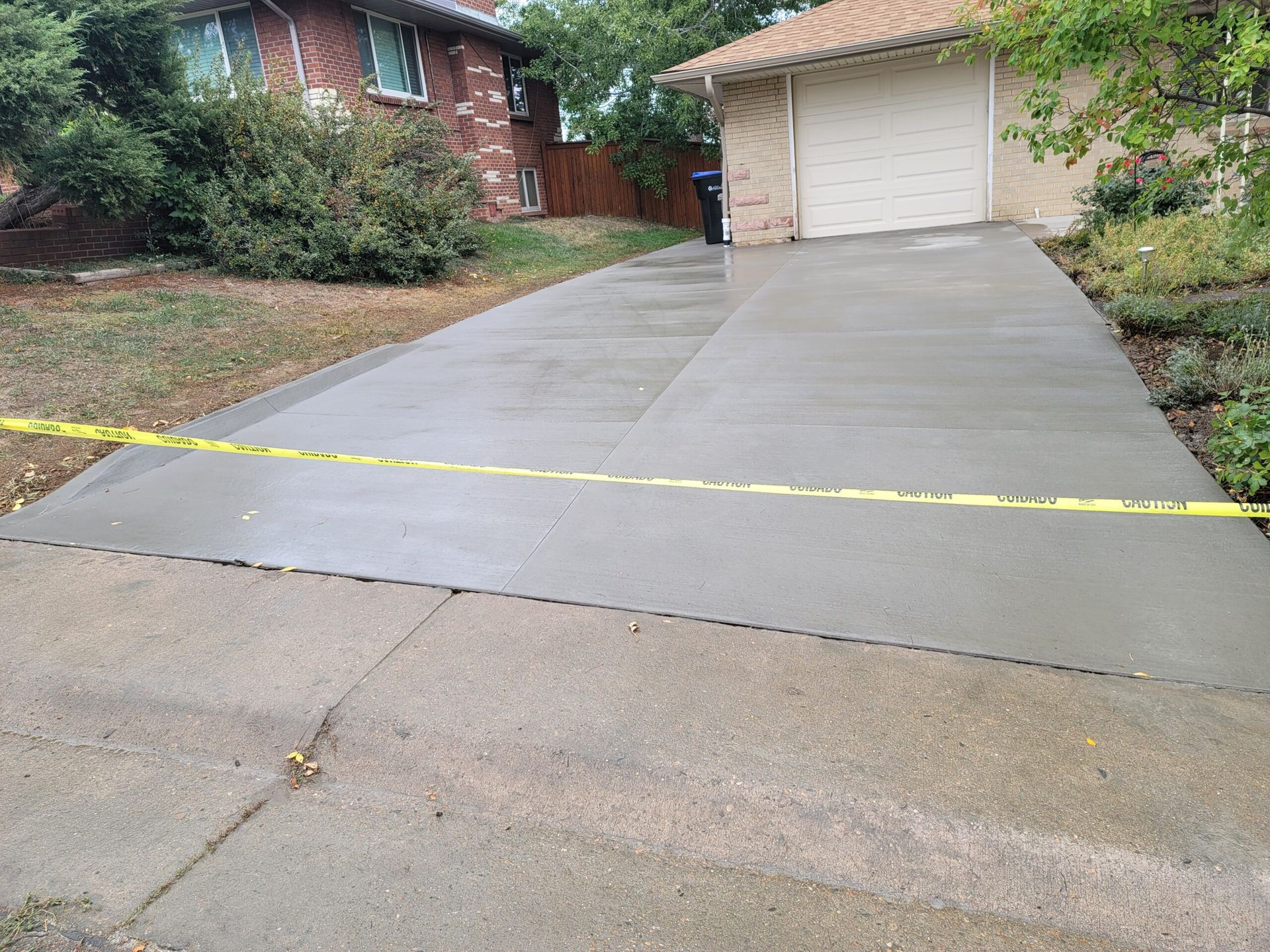 Concrete driveway blocked by yellow caution tape leading to a garage and brick house