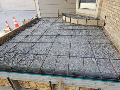 Concrete patio under construction with rebar mesh and formwork beside a house and garage