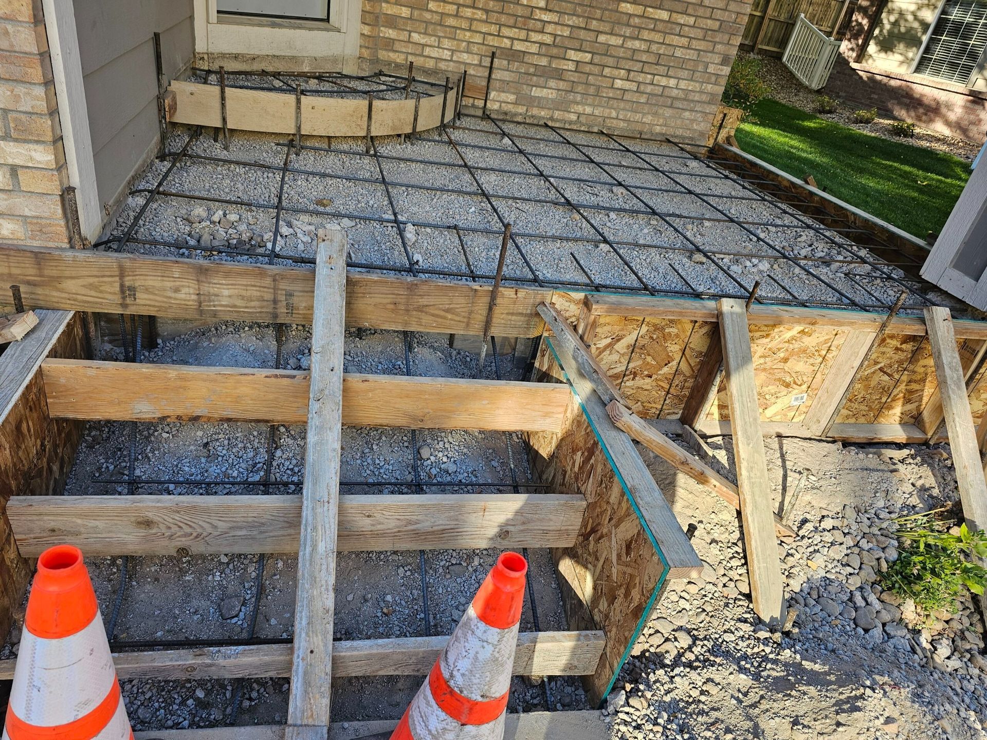 Partially demolished patio with exposed supports, concrete slab, and orange safety cones
