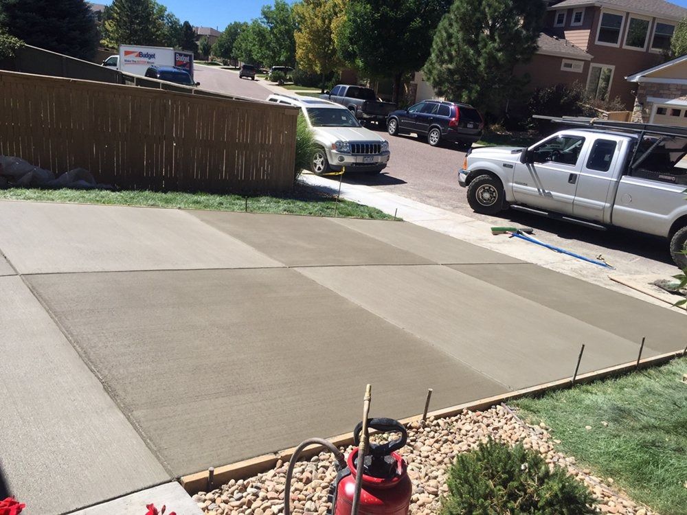 Concrete driveway with parked pickup trucks, a wooden fence, and a red weed trimmer in the foreground.