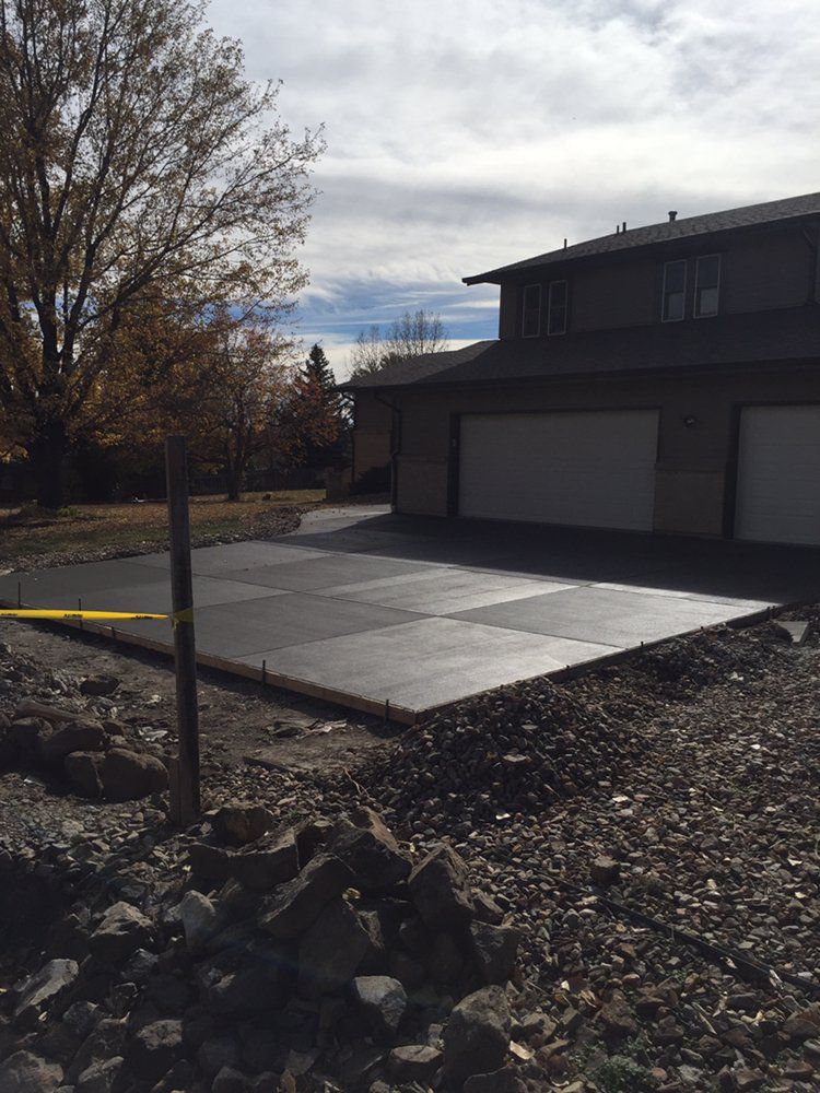 Residential driveway with fresh concrete slab beside a house and bare trees under a cloudy sky