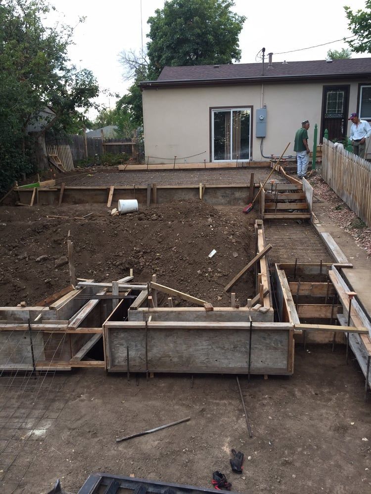 Backyard construction site with wooden forms and a trench in front of a house