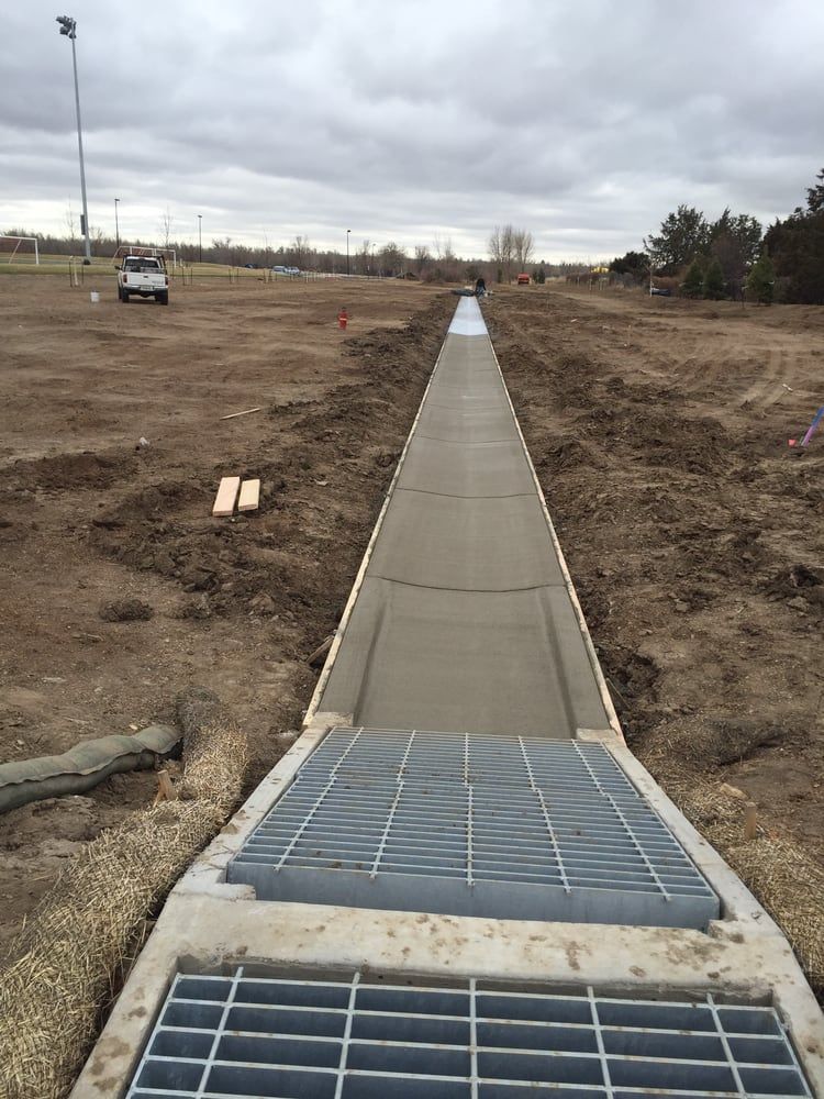 Long concrete sidewalk ending at a storm drain grate in a barren construction area