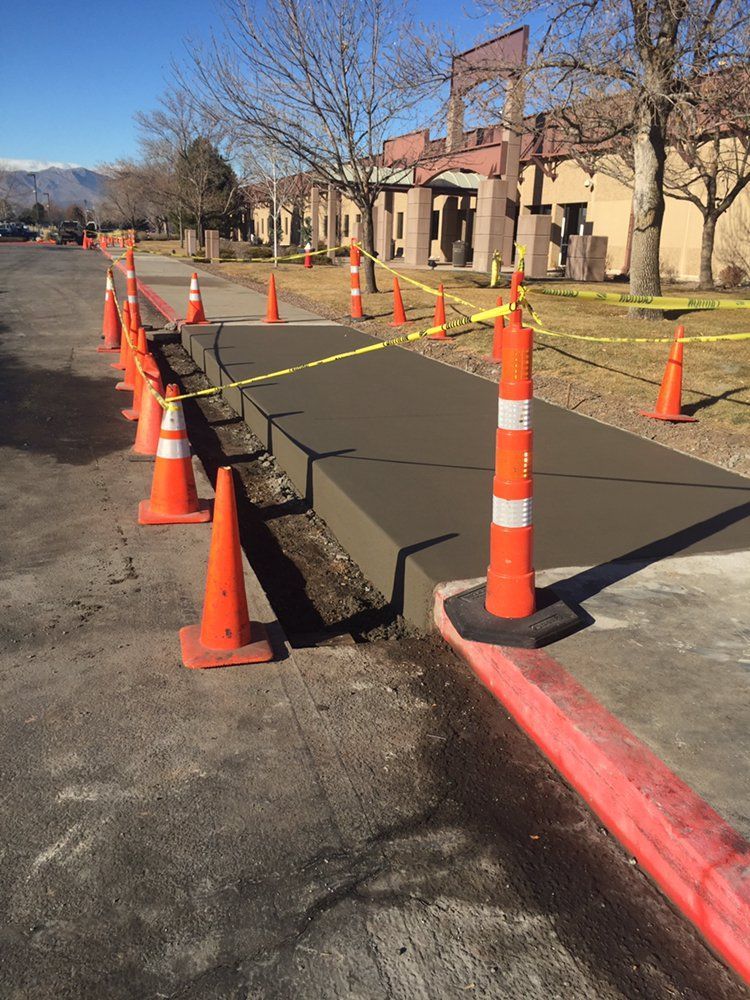 Orange cones lining a raised black walkway beside a building and curb on a sunny day