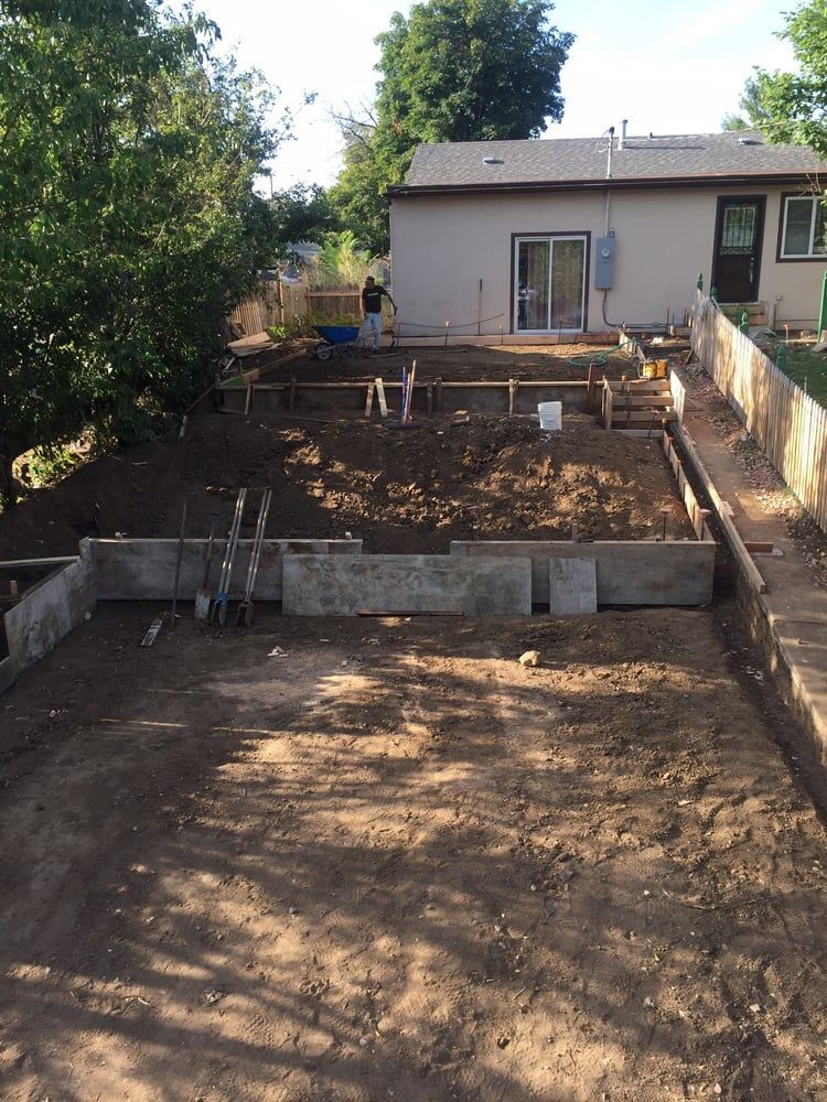 Backyard construction site with excavated dirt, retaining walls, and a house in the background