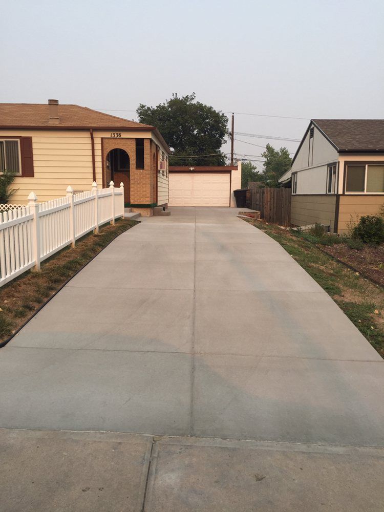Concrete driveway leading to a tan house with a white fence and garage at the end