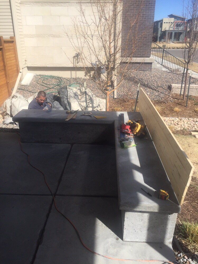 Man working on a rooftop beside a chimney, with black roofing material and tools in bright sunlight