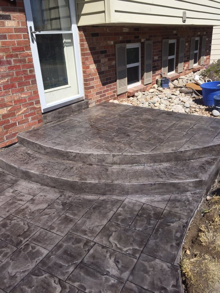 Stamped concrete patio and steps beside a brick house, leading to a white back door.