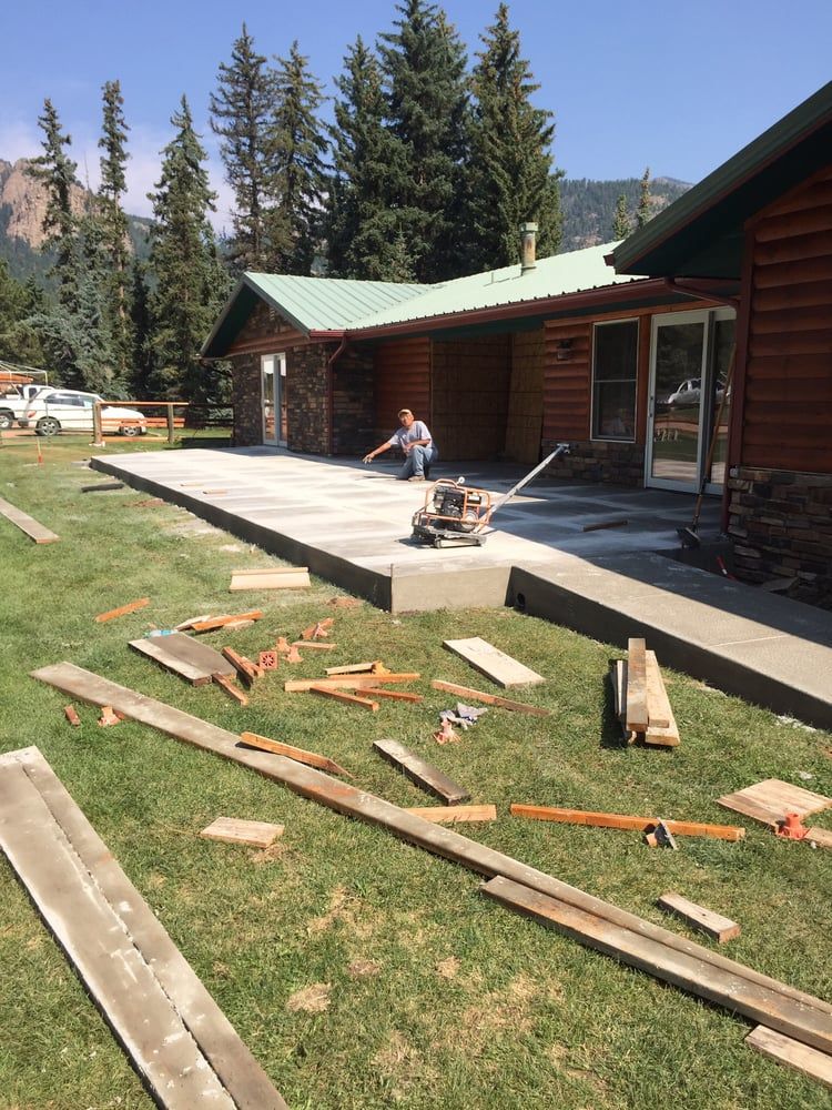 Cabin porch under repair, with lumber scattered on the lawn and a worker sitting on the deck